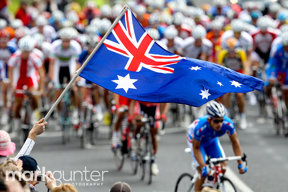 The peloton race below an Australian flag during the mens under 23 road race.
